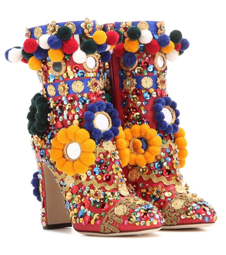 a pair of red ankle boots with high heels. the boots are heavily embellished with colorful sequins, pom poms, and mirrored flowers. the boots have a gold trim and a luxurious look. they are perfect for a party or a special occasion.