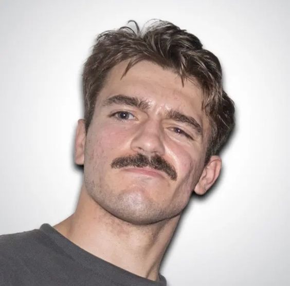 a headshot of a man with brown hair and a mustache, looking at the camera.