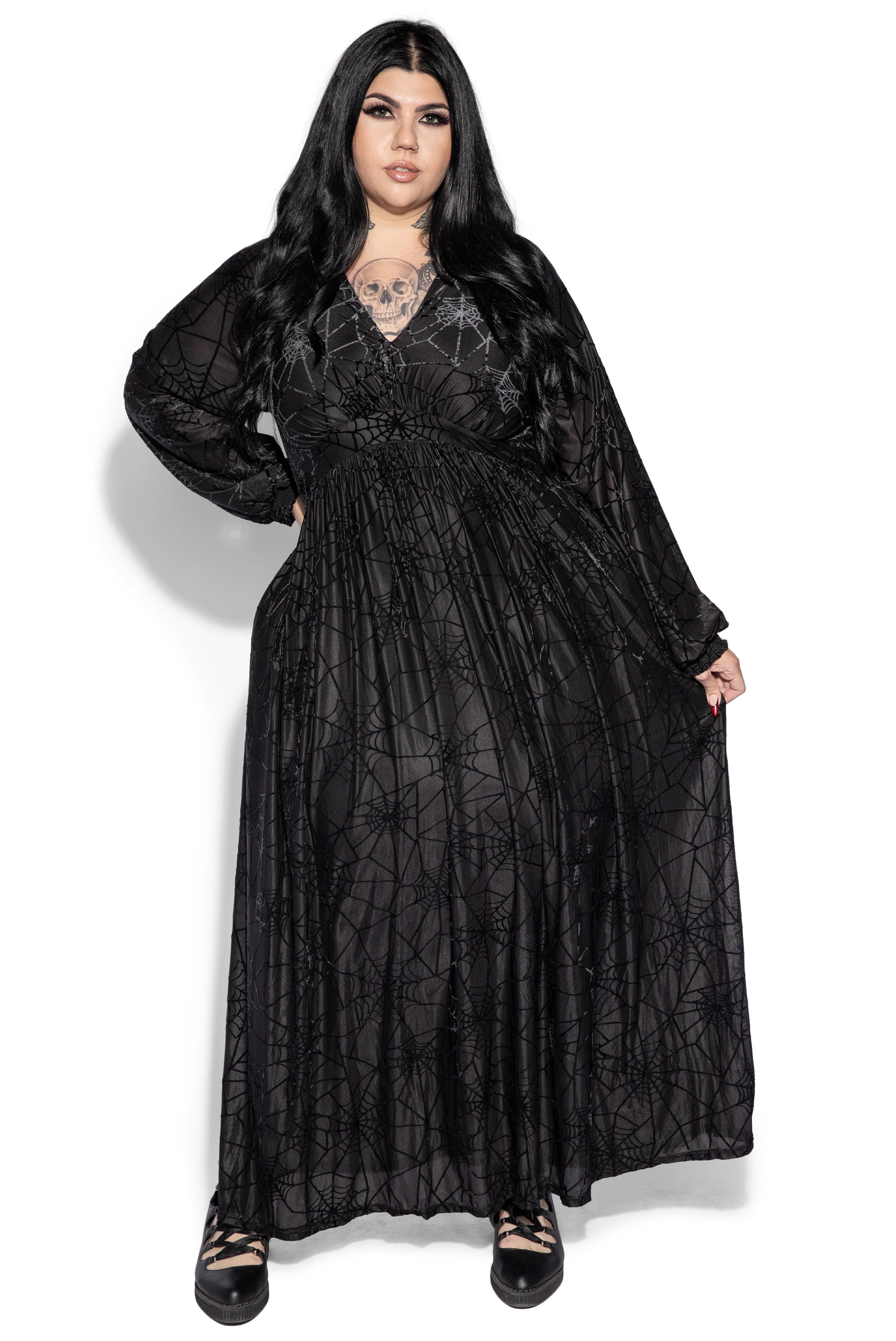 a fulllength studio shot showcases a plussize model wearing a striking black maxi dress. the dress features a long sleeve design, a pleated skirt, and a subtle yet prominent spiderweb pattern. the fabric appears to be a blend of velvet and a sheer overlay creating texture and depth. the model's dark hair and makeup complement the dress's gothic aesthetic, creating a stylish and darkthemed look, ideal for halloween or alternative fashion enthusiasts. the dress is flowing and drapes well on the model's figure.