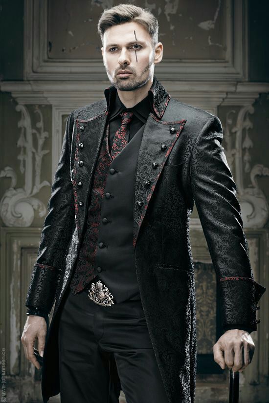 a man in a gothic fashion suit stands confidently, his hand resting on a cane. he wears a black dress shirt and patterned vest, complemented by a black and red patterned coat and tie. a decorative silver buckle adorns his waist. a scar marks his face, and the backdrop features ornate details, emphasizing the dark and elegant aesthetic.