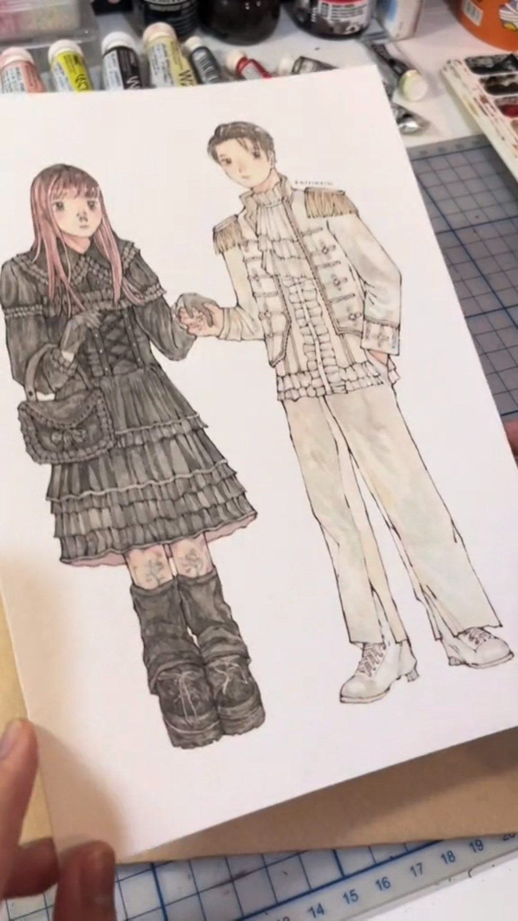 a drawing of an anime couple. the girl is dressed in gothic lolita fashion, with a black dress and boots. the boy is dressed in a white military style uniform with white pants and boots. they are holding hands and looking at each other lovingly. the drawing is done in a realistic style, with detailed shading and intricate clothing designs.