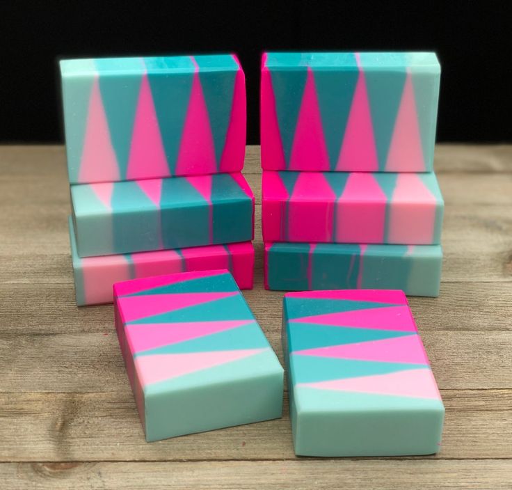 a collection of handcrafted soaps in teal, pink, and turquoise. the soaps are stacked in a pyramid shape, with the largest soap at the top. the soaps are all different sizes and shapes, and they have a variety of patterns. the soap is handmade and natural. the soaps are colorful and beautiful. they are perfect for a relaxing bath or shower.