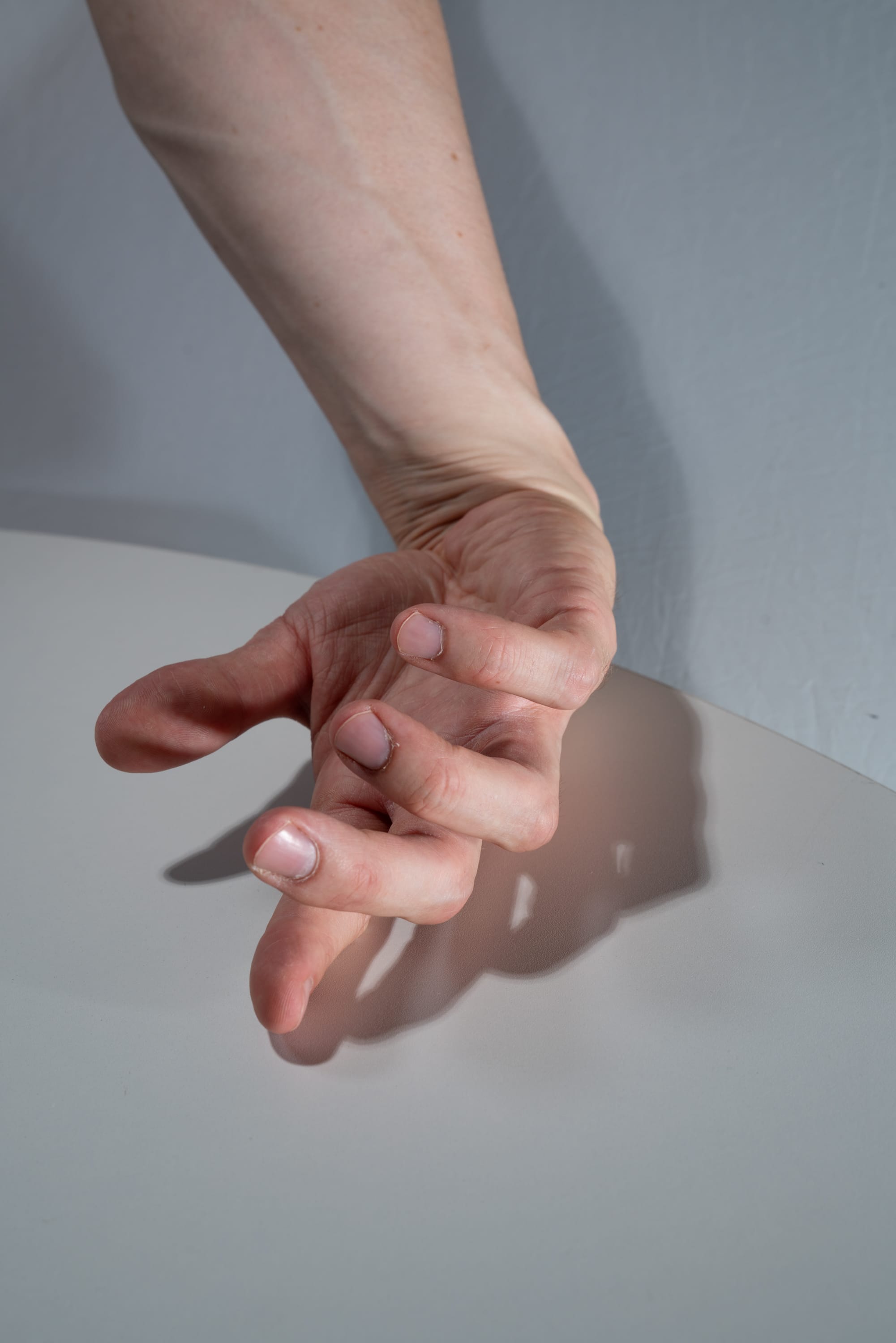 a closeup of a caucasian hand is shown with fingers spread out against a white table with a soft shadow cast on the right.