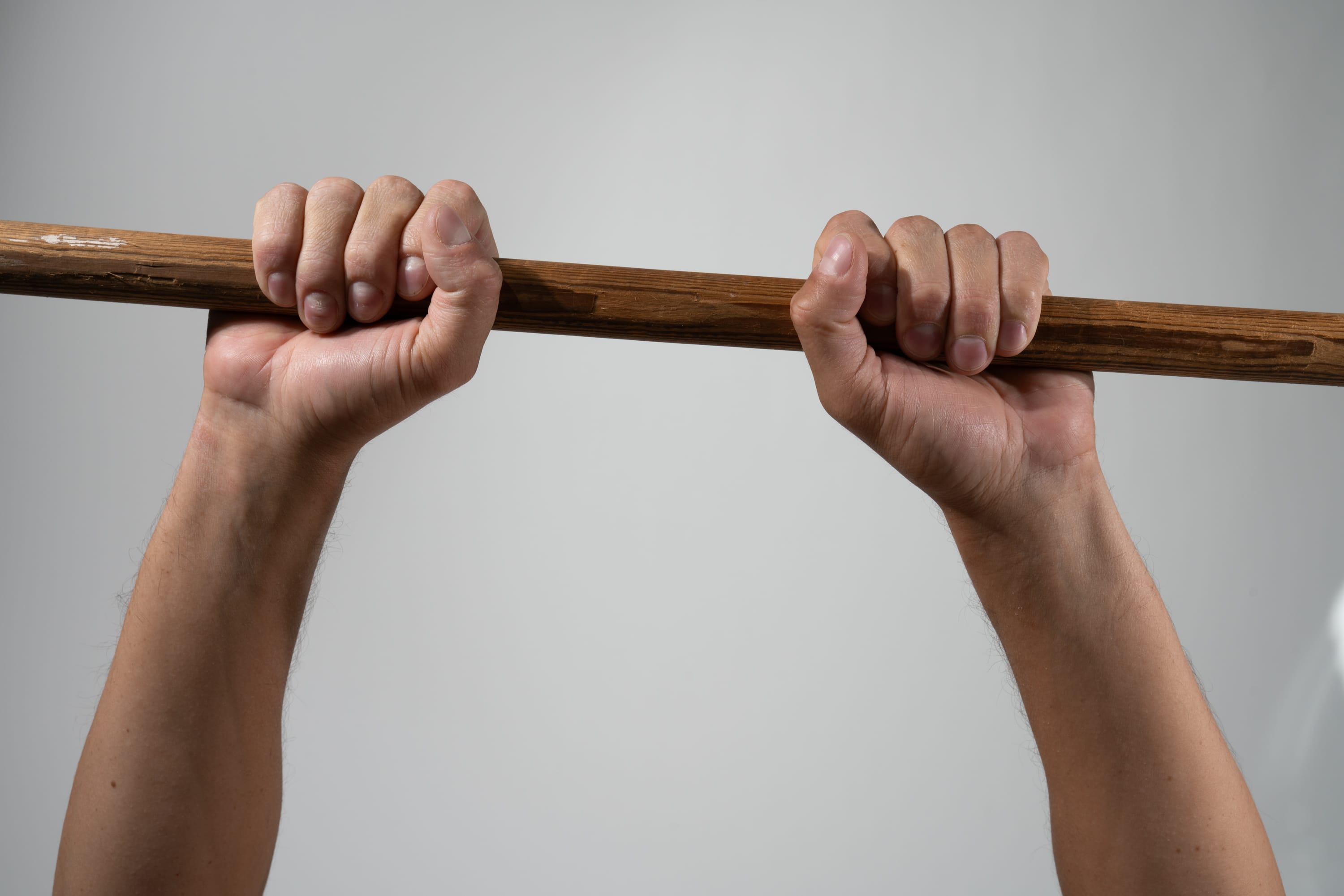a closeup shot of a man's hands gripping a wooden stick. the man's arms are extended upwards, and the image is taken from a low angle. the lighting is soft and diffused.