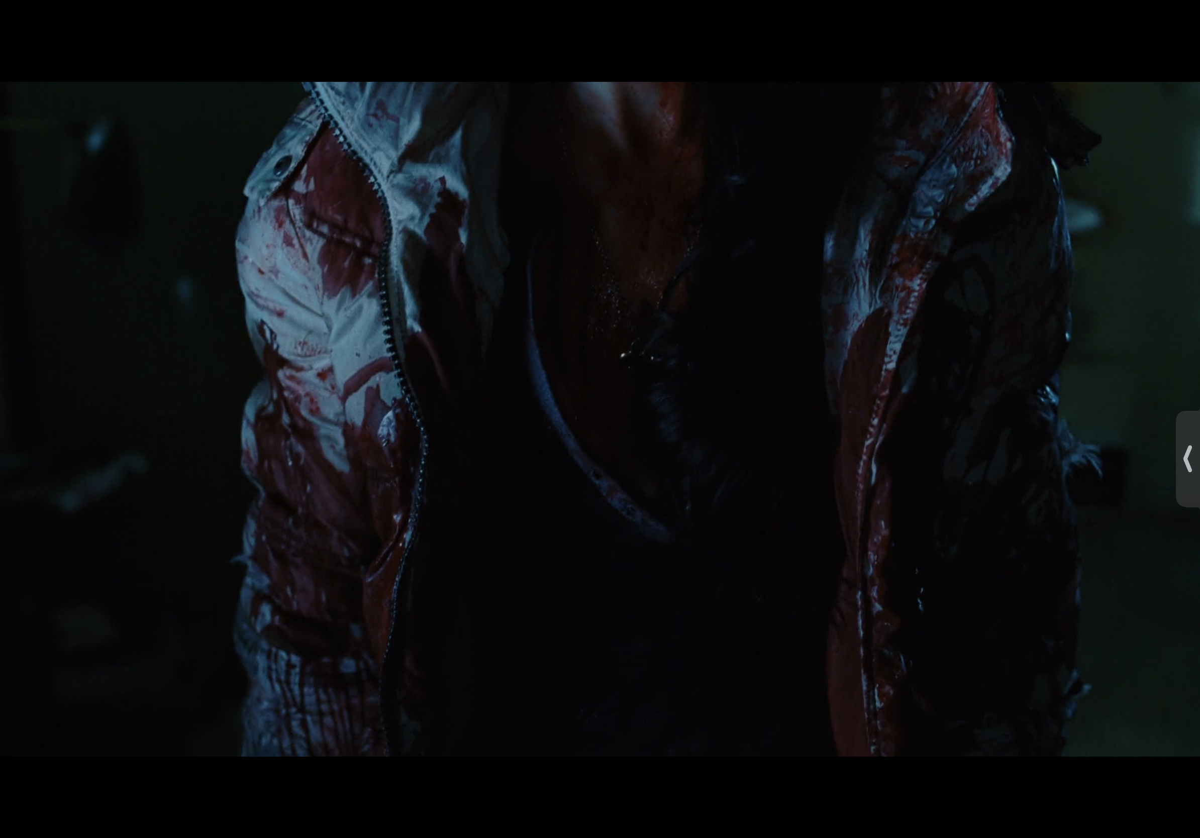 a closeup shot of a woman covered in blood, standing in a dark room.  the woman is wearing a white jacket with a red zipper, and there is a lot of blood on her jacket. the woman’s  face isn’t visible in the image, but  the red blood on the jacket suggests that she may have been injured. there are other unidentified objects in the background. the scene is very dark and there are very few details available, but it suggests violence or a crime.