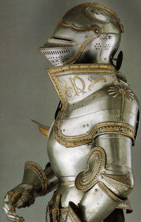 a closeup view of an ornate suit of plate armor, likely dating back to the renaissance period.  the gleaming metal is polished to a high shine, highlighting the intricate details of the helmet, breastplate, and gauntlets. the armor is adorned with decorative engravings and gold accents. the background is a neutral gray, drawing the viewer's focus entirely to the craftsmanship and artistry of the armor itself.