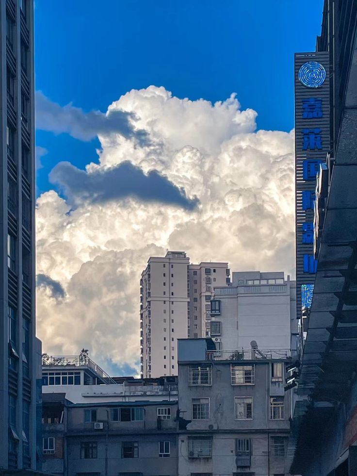 the image shows a cityscape with various buildings, including apartment buildings and skyscrapers, against a backdrop of a blue sky filled with fluffy white clouds. the buildings are of different heights and styles, creating a varied urban landscape. the image is taken from a somewhat low angle, looking up towards the sky.