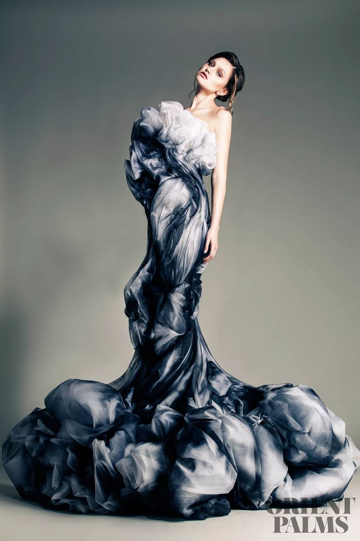a woman model poses dramatically wearing an elegant black and white  gown, in a studio with a grey background. the gown is made of flowing fabric and has a dramatic, almost artistic, feel. the model's pose and the gown's design create a stunning visual effect. the photographer has done a great job of capturing the model's beauty and the gown's unique design.
