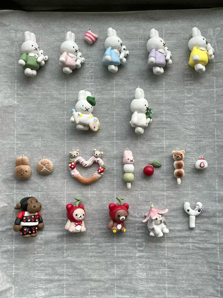 the image displays a collection of handmade charms, likely crafted from polymer clay. the charms feature various designs, including bunny figures reminiscent of miffy, bear characters like rilakkuma, and miniature food items such as dango and bread. these charms are likely intended for jewelry making or as decorative accessories. they are arranged on a gray surface, possibly parchment paper on a baking sheet.