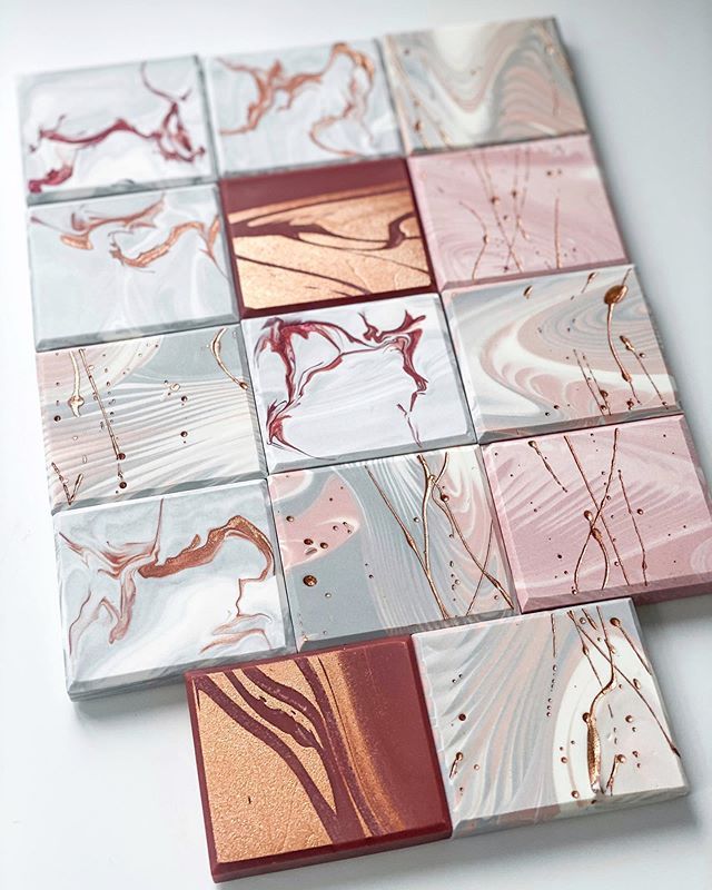 a close up of a collection of handmade marble coasters, featuring shades of gray, white, pink, brown and copper. the coasters are arranged in a square pattern, with the copper and pink tiles prominently in the foreground. the marble effect adds a touch of elegance and sophistication to the coasters.