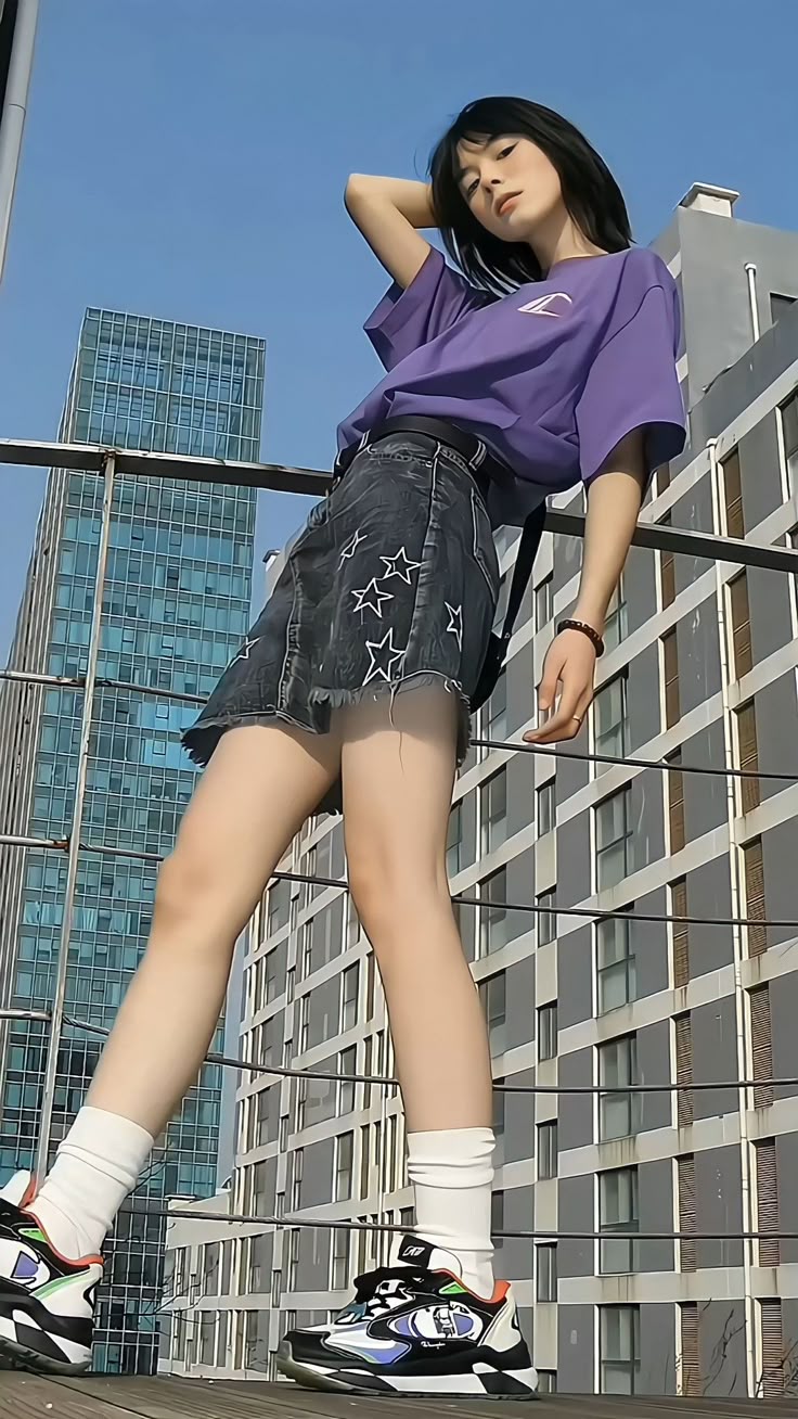 a young woman poses for a photo in an urban setting. she is wearing a purple tshirt, a black denim skirt with star designs, white socks, and colorful sneakers. she is leaning against a metal railing with modern buildings in the background and a blue sky above. her pose and clothing suggest a casual and fashionable style.