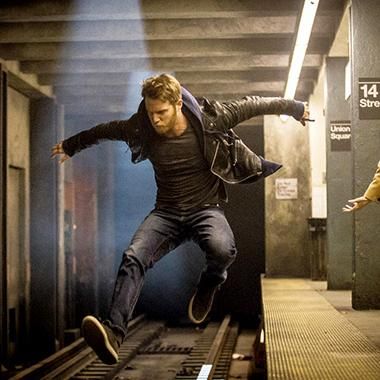 a man in a leather jacket and jeans jumps over train tracks in a subway station. the man is in motion, his body blurred as he leaps over the tracks. the station is dimly lit, with the platforms and walls visible in the background. the man's determined expression and energetic movements convey a sense of urgency and excitement. the image captures a moment of dynamic action, showcasing the energy and speed of urban life.