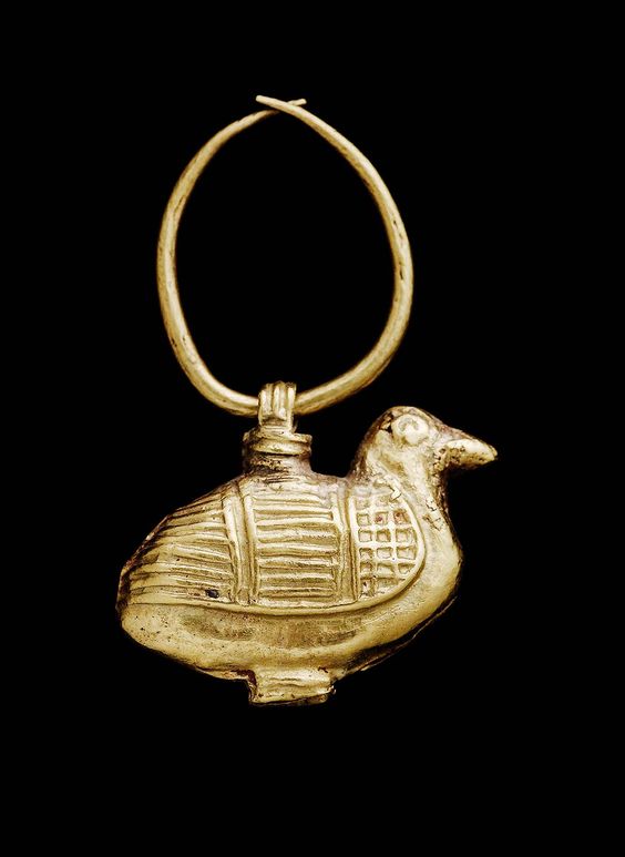 a gold pendant shaped like a small bird. the bird's body is decorated with lines and squares, and it has a small loop at the top for hanging. the background is solid black.