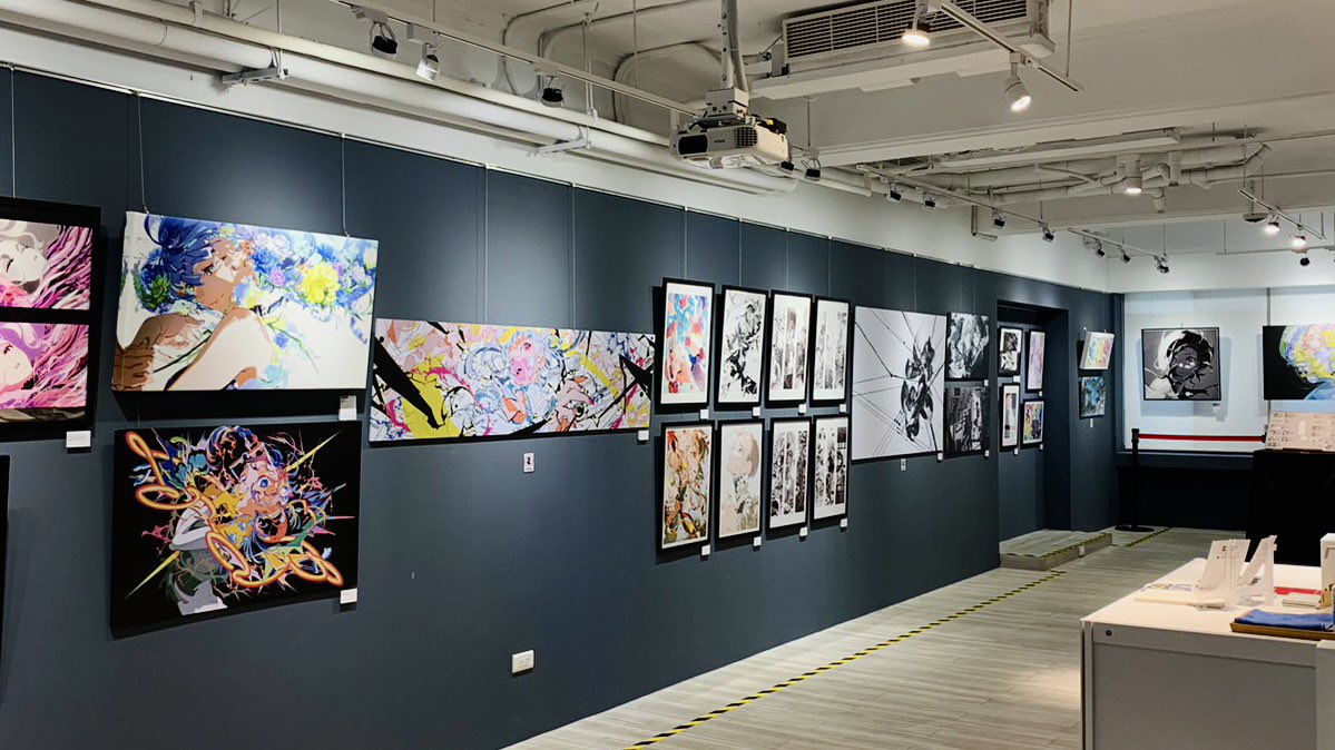 the image shows the interior of an art gallery with a variety of colorful, modern artworks on display. the paintings are mounted on a dark gray wall and illuminated by spotlights.  the gallery space is empty, creating a sense of anticipation.