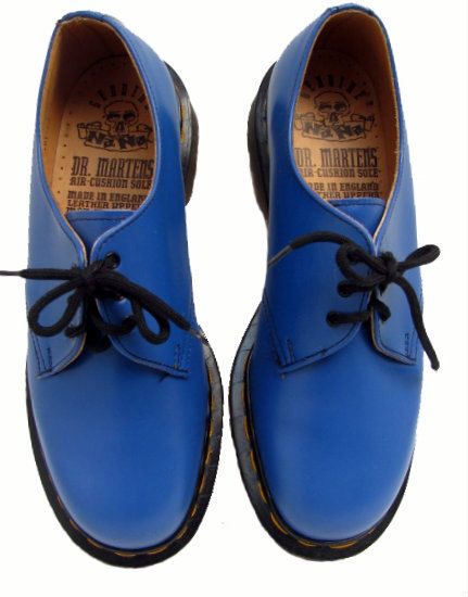 a pair of blue dr. martens shoes with black laces are shown from a topdown perspective. the inner soles are visible, displaying the brand's logo and "air cushion sole made in england leather upper". the shoes have a classic, rounded toe design with visible stitching and a thick, black sole with yellow accents.