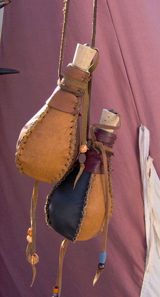 two leather pouches hang from a rope. the pouches are various shades of brown, blue and purple, and they are stitched together. they are closed with cork stoppers and adorned with beads.