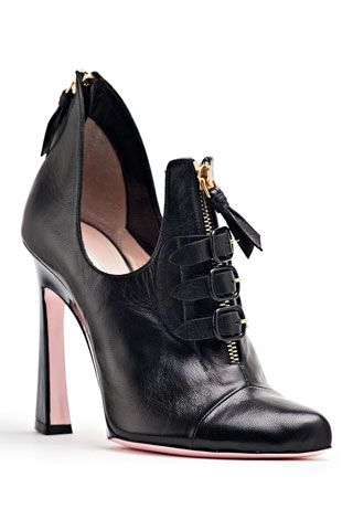 a single black leather high heel shoe is shown on a white background. the shoe features a zipper down the front, adorned with small buckles. the heel has a pink accent color. the style is contemporary and fashionable.