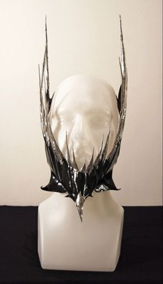 a black and silver fantasy crown sits upon a white styrofoam head.  the crown has a tall point in the front and two tall, pointed "wings" that sweep back from the front point.  the points are silver and appear to be made of a shiny material, possibly metal.  the base of the crown is a black material, possibly leather.  the background is white.