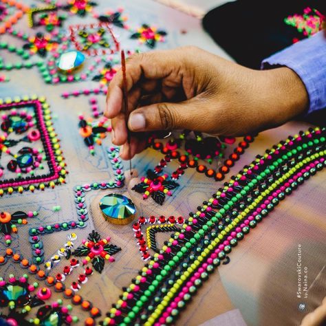 a close up image of a hand meticulously beading an intricate pattern with colorful beads and sequins. the image highlights the craftsmanship and artistry involved in creating handmade clothing with intricate details. the beads and sequins create a sparkling and eyecatching design that adds a touch of glamour and sophistication. the image captures the beauty and intricate detail of high fashion clothing.