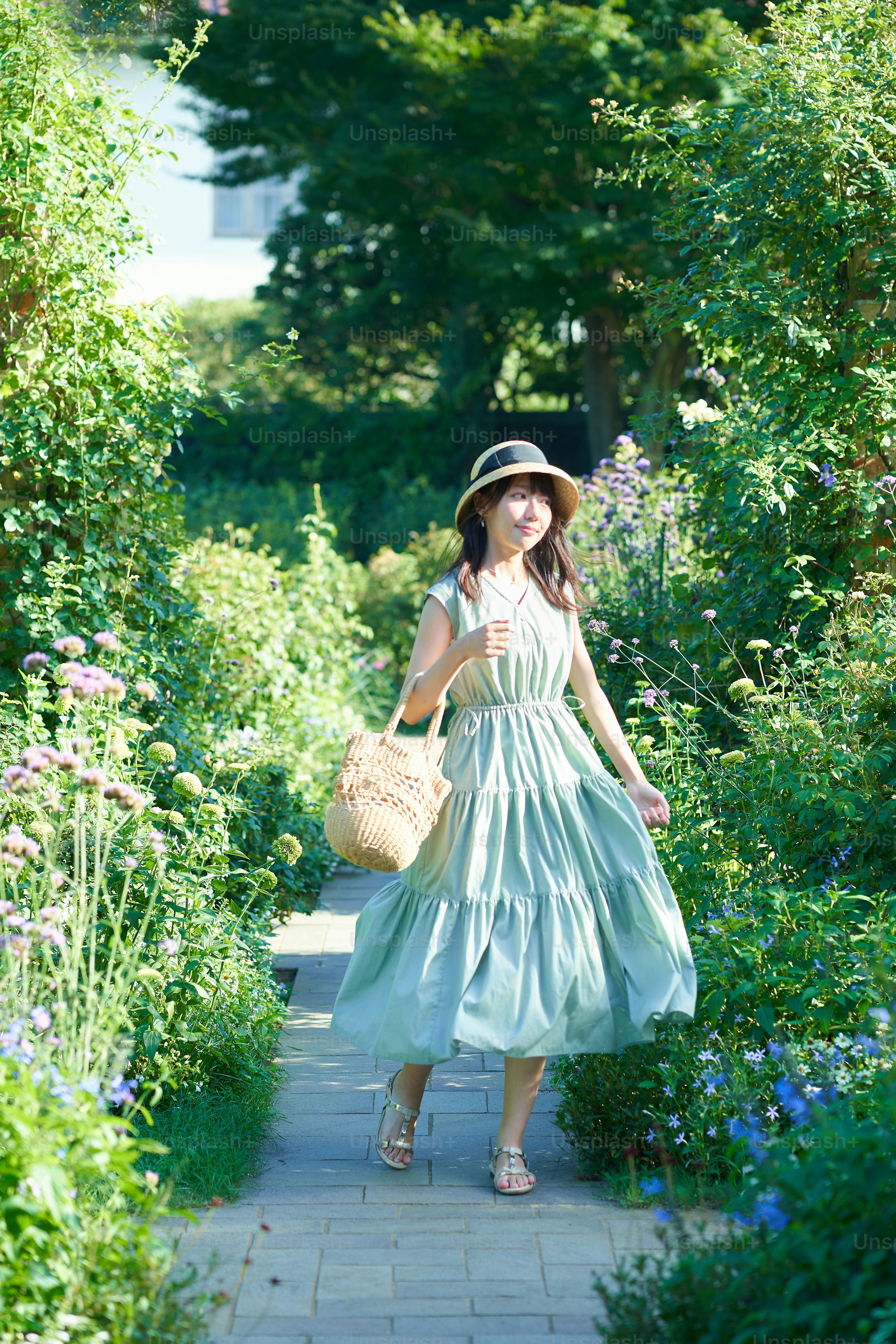 a young woman in a light green summer dress and straw hat is happily strolling down a garden path surrounded by lush green plants and flowers.  she carries a woven bag and appears joyful and relaxed in the sunny outdoors.  the scene evokes a sense of summer peace and contentment.
