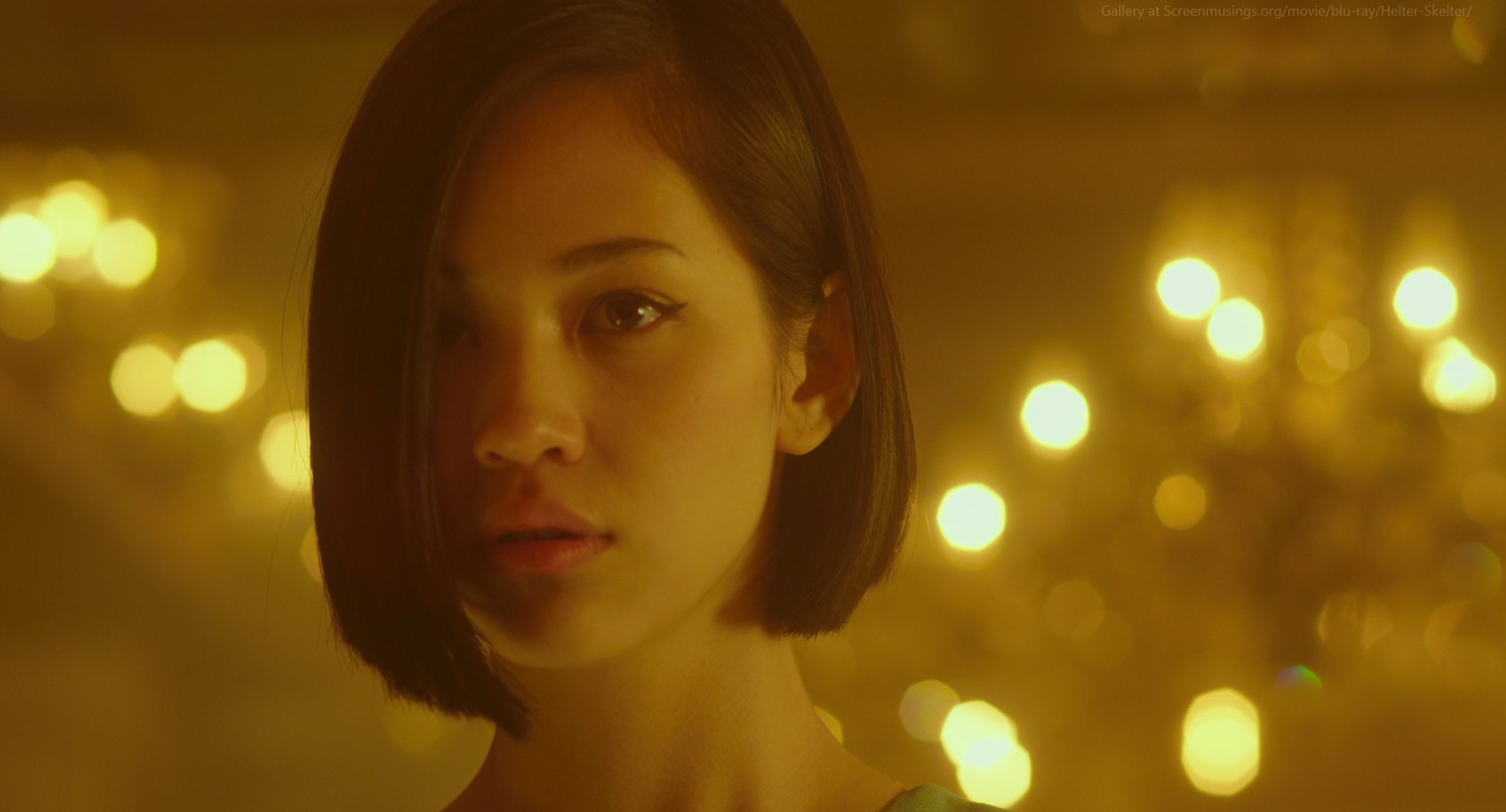 a young woman with short, dark hair is the focus of this portrait. she has a neutral expression and is looking directly at the viewer. the background is blurred, with warm yellow lights creating a bokeh effect. the overall feeling of the image is cinematic and atmospheric.