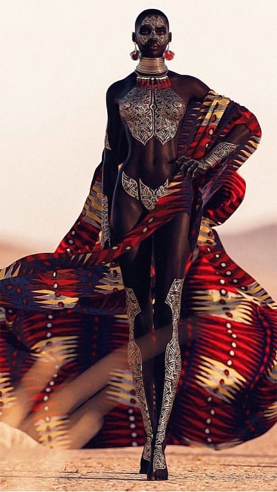 a woman in a patterned, tribal outfit stands in a desert setting.  she is painted with tribal markings and wears jewelry.  her hair is pulled back off her face and she looks directly at the viewer.