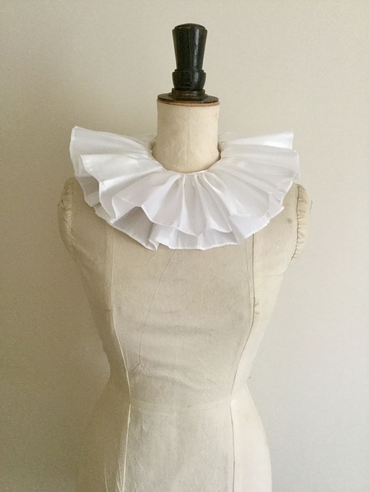 a closeup shot of a beautiful white pleated ruffle collar displayed on a dress form. the collar is meticulously crafted with delicate pleats, creating a luxurious and elegant appearance.  the dress form is a simple, offwhite color, allowing the collar to be the focal point of the image. the background is a plain, light beige wall, providing a neutral backdrop that emphasizes the collar's intricate detail.  the overall impression is one of refined style and quality craftsmanship.