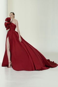 a woman in a beautiful red gown with a oneshoulder design, a long train, and a bow on the shoulder poses gracefully. the dress is a showstopper with its elegant design and bright color. the woman is wearing simple makeup and accessories, letting the dress take center stage. she looks confident and elegant, ready for a special event.