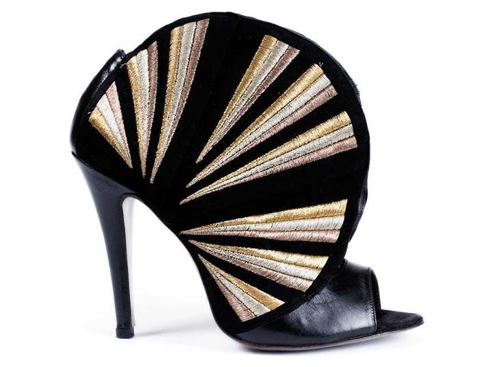 a black peep toe high heel shoe with gold and metallic embroidery is seen in a studio shot on a white background. the shoe has a black stiletto heel. the upper part of the shoe is decorated with a design resembling rays emanating from the base of the heel. the rays are embroidered in gold and metallic threads. the shoe's peep toe is open. the overall style of the shoe is fashionable and decorative.