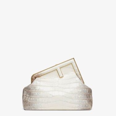 a white alligator skin clutch handbag with gold trim and a fendi logo sits against a white background.