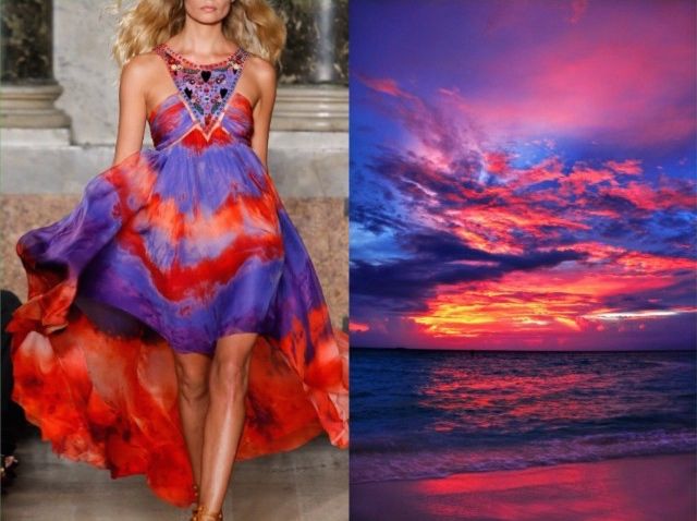 a woman in a flowing purple and red dress with a beaded neckline stands in the left side of the image. the dress is tiedyed and the woman is wearing heels. the right side of the image is a colorful sunset over the ocean with beautiful clouds. the scene is very colorful.