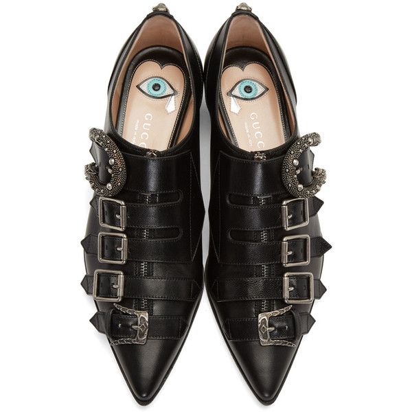 a pair of black gucci women's shoes are shown in the image.  the shoes are pointedtoe flats made of leather. they feature multiple buckles and are embellished with snake and evil eye details. the inside of the shoes show the gucci logo.  the shoes are presented from a topdown perspective against a white background.