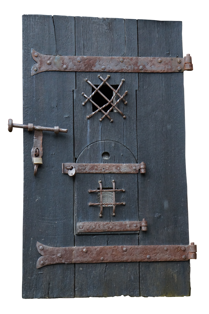 a closeup shot of an old, dark, wooden jail door. the door is made of vertical planks held together by three horizontal, rusty, metal straps with rivets. there are two small barred windows, one with a twisted metal grid and the other with a wire mesh. a slide bolt with a small padlock secures the door, and there is a round hole with a barred cover above the lower window. the door appears old and weathered.