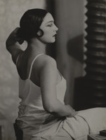 the image is a black and white portrait photograph of a young woman, possibly from the 1920s or 1930s. she is seated, her body angled slightly away from the camera, with her gaze directed to her right, away from the viewer. she has a classic bob hairstyle and is wearing a simple, lightcolored slip or camisole. her expression is serene and thoughtful. the background is blurred and indistinct, drawing focus to the subject. the lighting and shadowing create a dramatic and artistic effect, characteristic of vintage portrait photography. the overall mood is one of quiet elegance and timeless beauty.