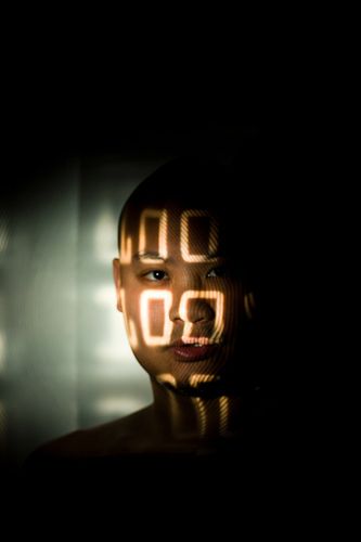 a close up, lowlight, mysterious portrait of a woman. her face is mostly in the dark, but light shines through her face highlighting her features.  the light makes it appear like numbers are projected onto her face.