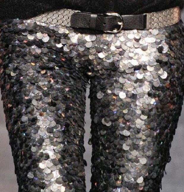 a close up shot of black and silver sequin pants. the pants have a belt with a silver buckle. the sequins are arranged in a pattern that resembles scales. the pants are very shiny and sparkle.