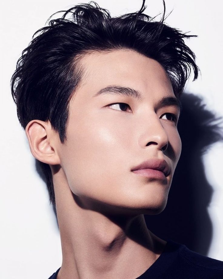 the image is a closeup, stylized portrait of a young asian male model. he has dark, styled hair with a slightly tousled look. his skin is exceptionally smooth and clear, suggesting the image might be related to skincare or beauty products. the lighting is moody, with shadows accentuating his facial features. the overall style is elegant and sophisticated. the model is looking off to the side and slightly upward, revealing a strong jawline and neck. the background is simple and unobtrusive, focusing all attention on the model.