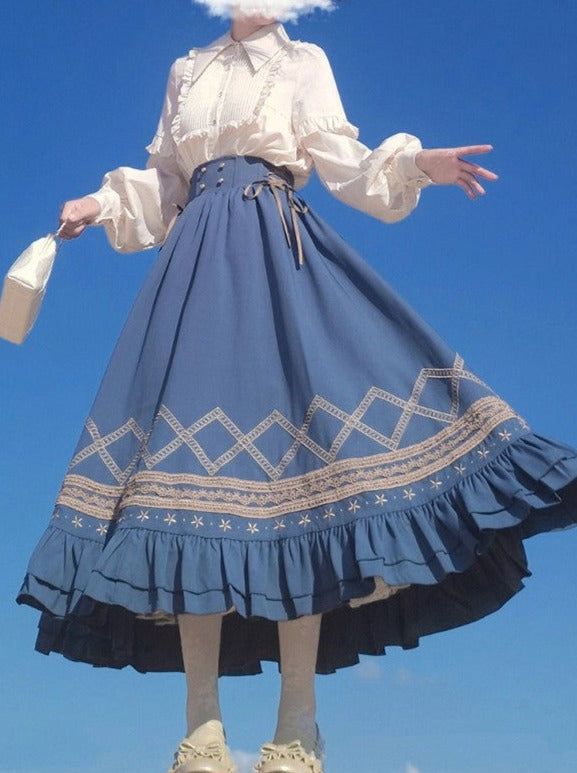 a woman wearing a white blouse with ruffled details and a long, aline blue skirt with decorative embroidery and ruffles, standing against a bright blue sky. she holds a small handbag and wears ivorycolored shoes with kneehigh socks.