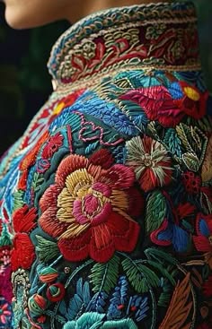 a closeup shot of a richly embroidered garment with intricate floral motifs. the fabric is a dark blue background with colorful threads woven into intricate designs. the colors are vibrant and bold, and the craftsmanship is clearly evident. the detail of the flowers and leaves is impressive, and the garment looks like it is made with care and attention to detail.