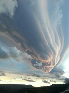 a stunning view of a dramatic sky filled with swirling clouds. the clouds are a light, almost translucent grey and are arranged in a series of overlapping swirls and folds. they appear as if they are forming a large, intricate sculpture in the sky. the clouds are illuminated by the setting sun, casting long shadows on the land below. the image is a reminder of the power and beauty of nature.