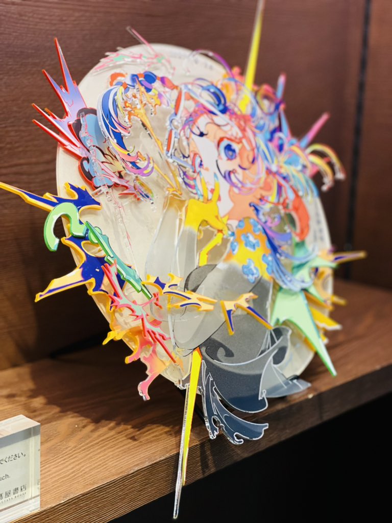 a colorful acrylic sculpture of an anime character is displayed on a wooden shelf. the artwork features a vibrant and dynamic composition with abstract shapes and patterns.