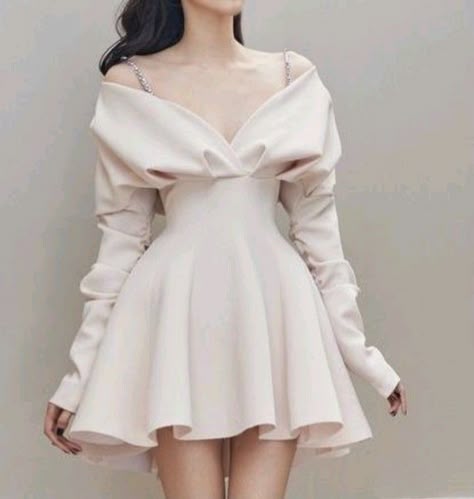 a woman in a white, short, vneck dress with long sleeves is posing in a studio. the dress is fitted at the waist and flows out into a slightly ruffled skirt. the model has her hair pulled back, showing off her makeup and the delicate jewelry she is wearing. the background is a simple white wall.