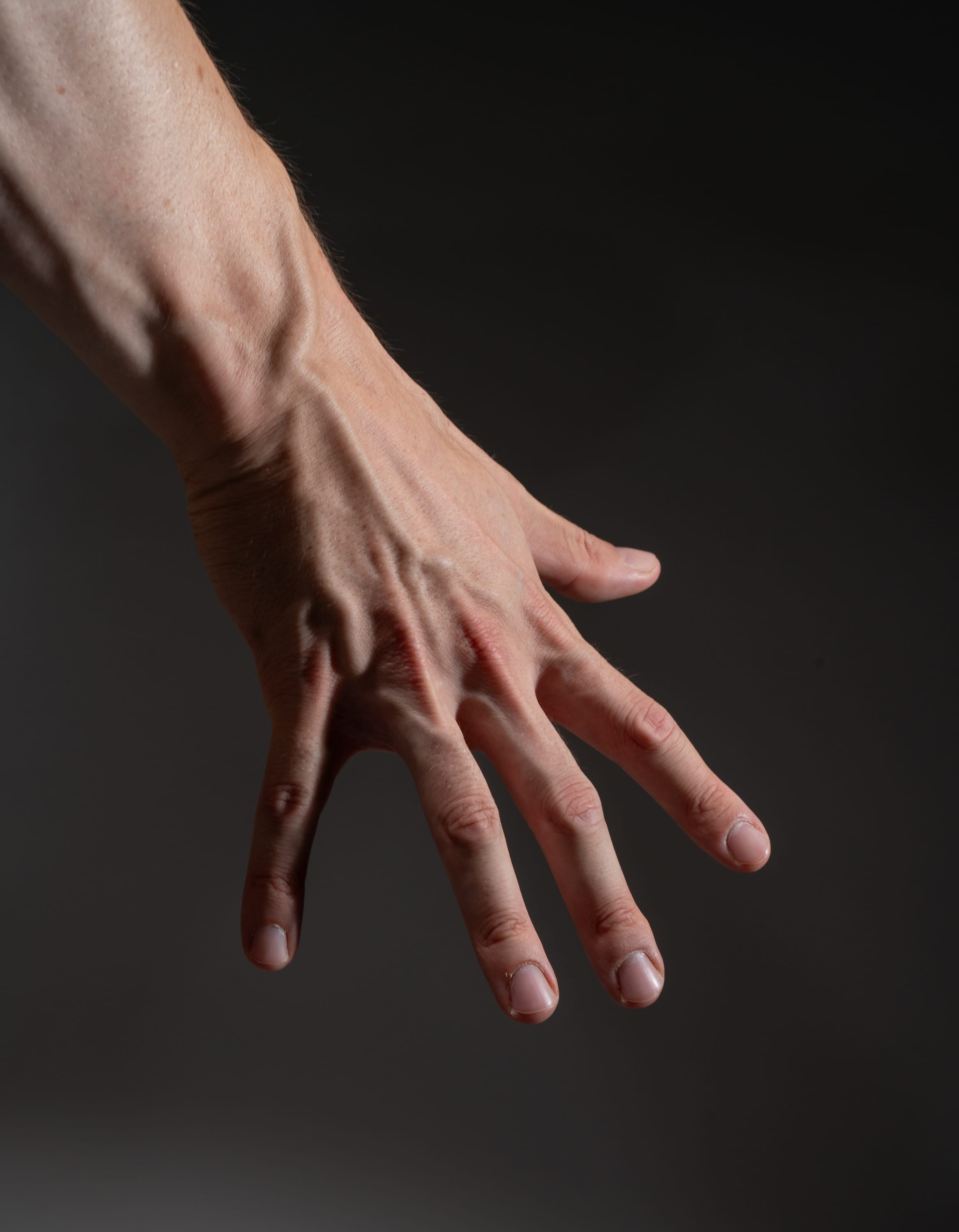 this is a closeup image of a man's hand and forearm against a dark background. the hand is extended with the fingers slightly curled. the veins on the hand and arm are prominent, giving a sense of strength and vitality.  the image is welllit, highlighting the texture and detail of the skin. the dark background provides a strong contrast, drawing attention to the hand.