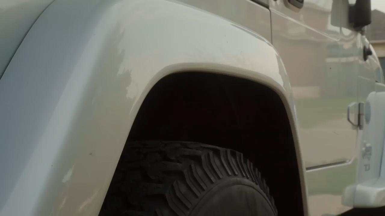 closeup view of a white car's exterior, showcasing the wheel well, tire, and a portion of the car's side.  the lighting suggests it's daytime.
