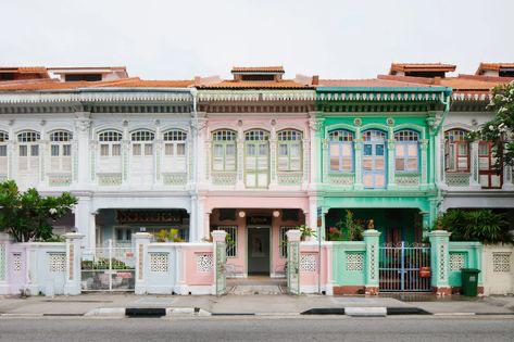 the image shows a row of four colorful shophouses in singapore.  these buildings are characteristic of peranakan architecture, with their distinctive pastel colors (teal, pink, and white), intricate details on the facades, and traditional window and door designs. the shophouses stand sidebyside, sharing a common architectural style and color palette that creates a visually harmonious and attractive street scene.  the scene is tranquil, with some small plants and trees in front of the buildings. the street in front is clean and appears to be in a residential area.