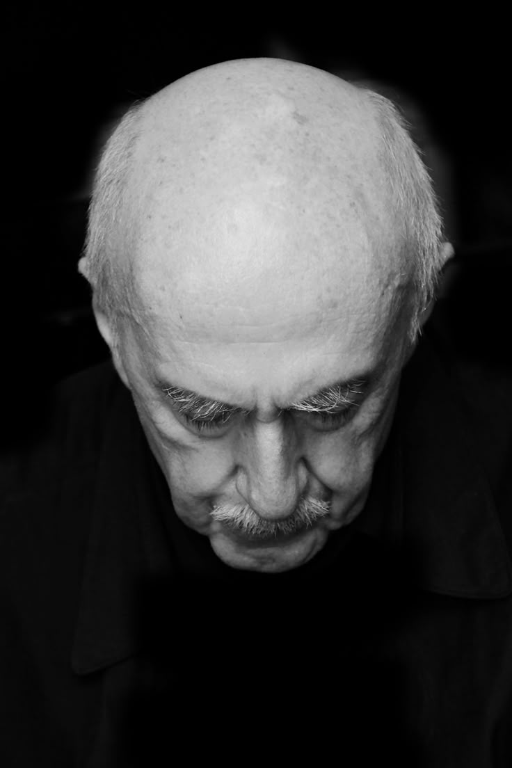 a black and white portrait of an elderly bald man with a mustache, looking down with a serious expression.