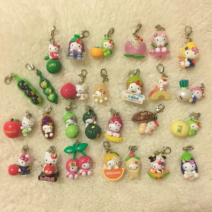 the image shows a collection of hello kitty keychains featuring various fruit and vegetable themes. the keychains are displayed on a fluffy white surface. each keychain features a hello kitty character incorporated into different types of fruits or vegetables.