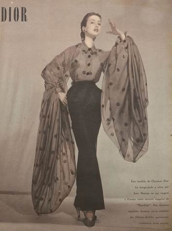 an vintage dior advertisement features a model in a stylish ensemble. the model wears a sheer, longsleeved blouse with a floral pattern and dark buttons, paired with a highwaisted, fitted black skirt that flares slightly at the bottom. the blouse's sleeves are dramatically draped, adding to the overall elegance of the outfit. she is wearing high heels, which are barely visible. the pose showcases the design, and the overall image has a classic, refined aesthetic typical of high fashion advertising of the era.