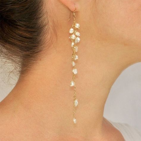 a closeup side view of a woman wearing a long, dangling gold earring with small white pearls. the woman has brown hair and a light complexion.  the earring is delicate and elegant.  she is wearing a white shirt. the lighting is bright and natural, highlighting the details of the earring and the woman's features.