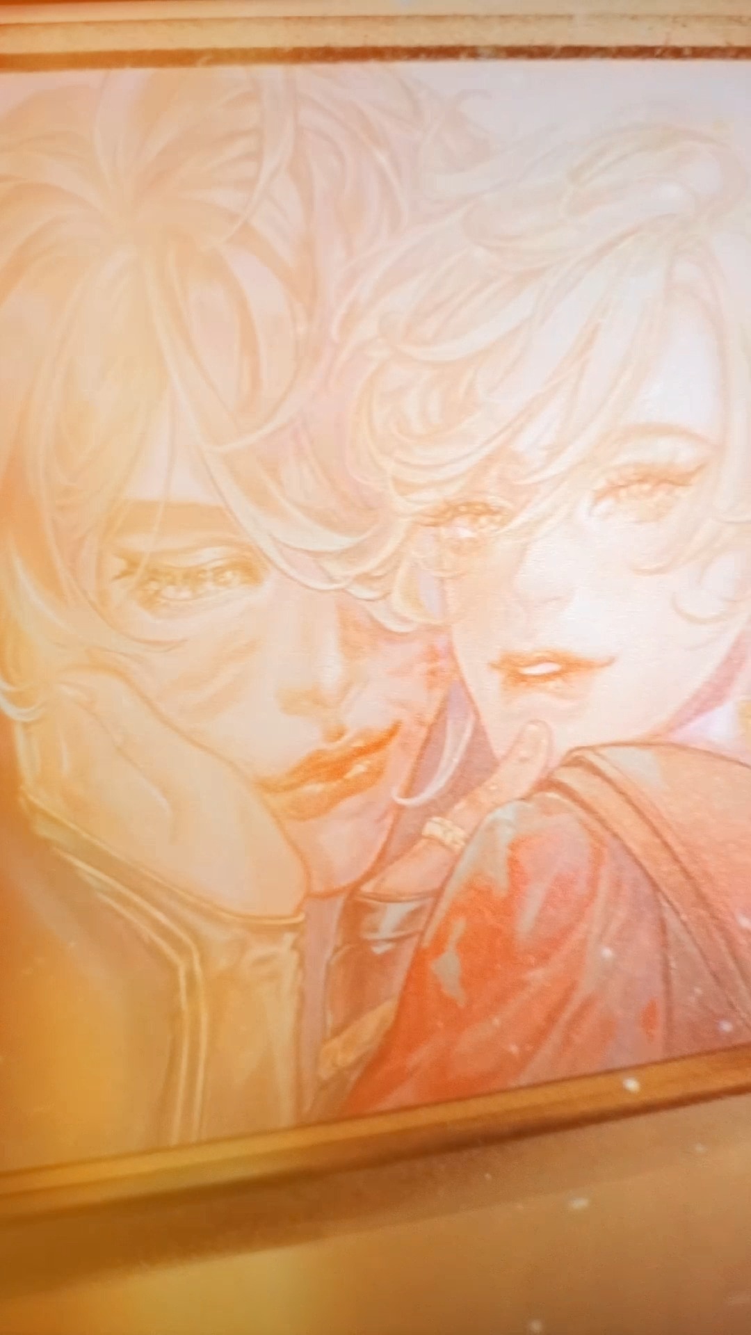 he image shows a closeup view of a framed painting depicting two individuals, possibly a couple, in an embrace.  the artwork is rendered in soft, pastel shades of orange and peach, creating a gentle and serene atmosphere.  the subjects have light, flowing blonde hair and their features are softly rendered, emphasizing a romantic and tender mood. the overall style is delicate and suggestive of a calm and intimate moment.
